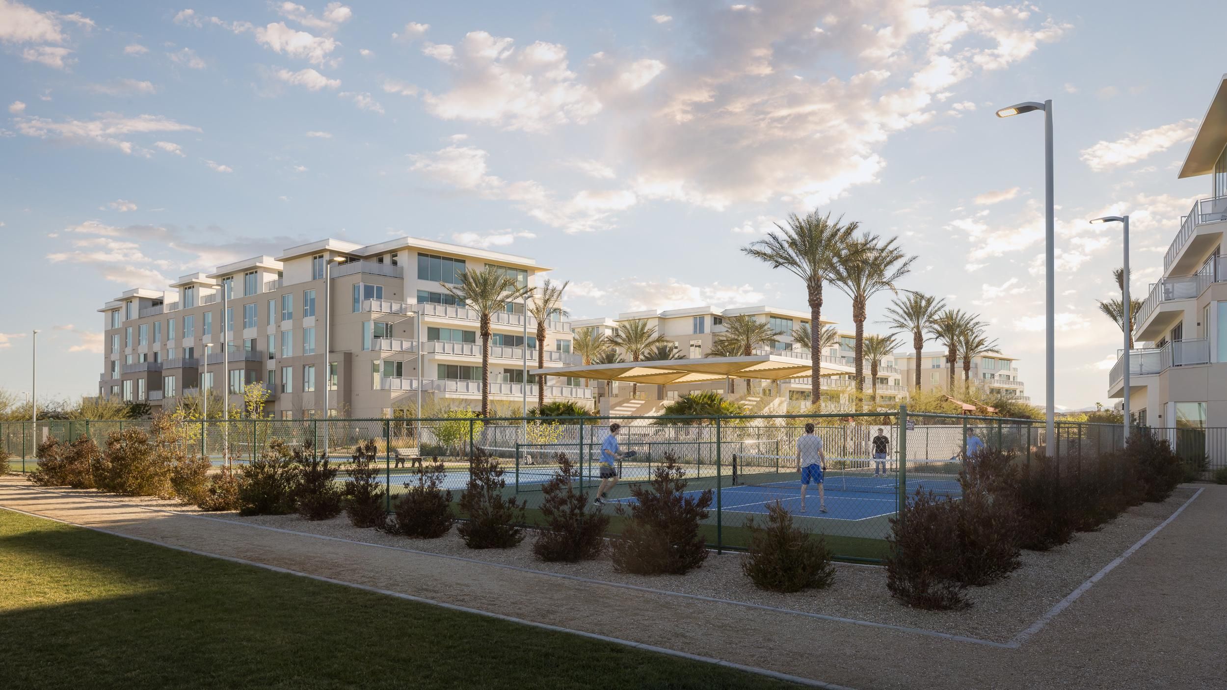 People play tennis on an outdoor court surrounded by palm trees and modern apartment buildings at sunset. Photo credit: Michael Tessler Photography.