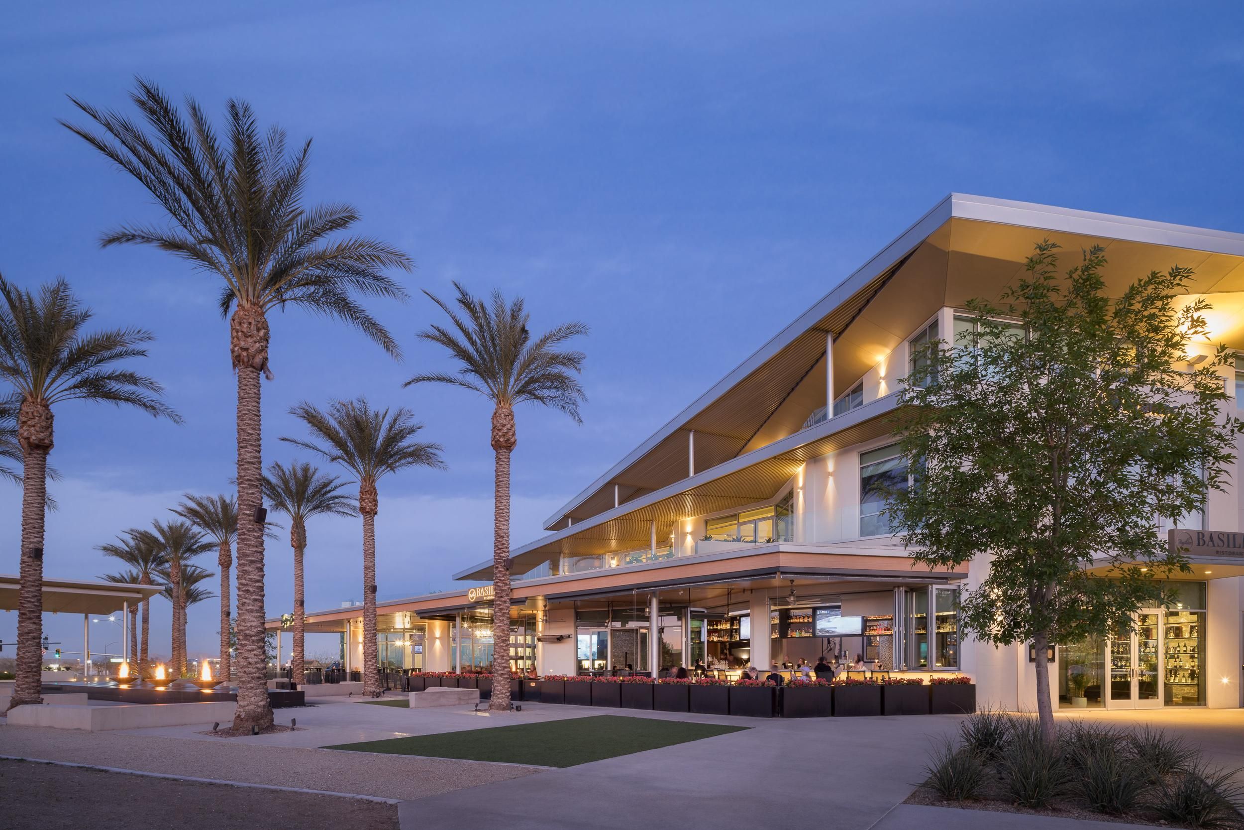 Modern building with large windows, palm trees, and outdoor seating at dusk under a clear, blue sky. Photo credit: Michael Tessler Photography.