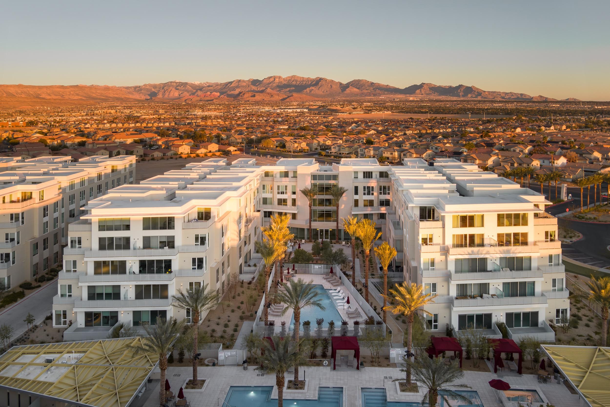 Aerial view of modern apartment buildings with pools, palm trees, and a city with mountains in the background at sunset. Photo credit: Michael Tessler Photography.