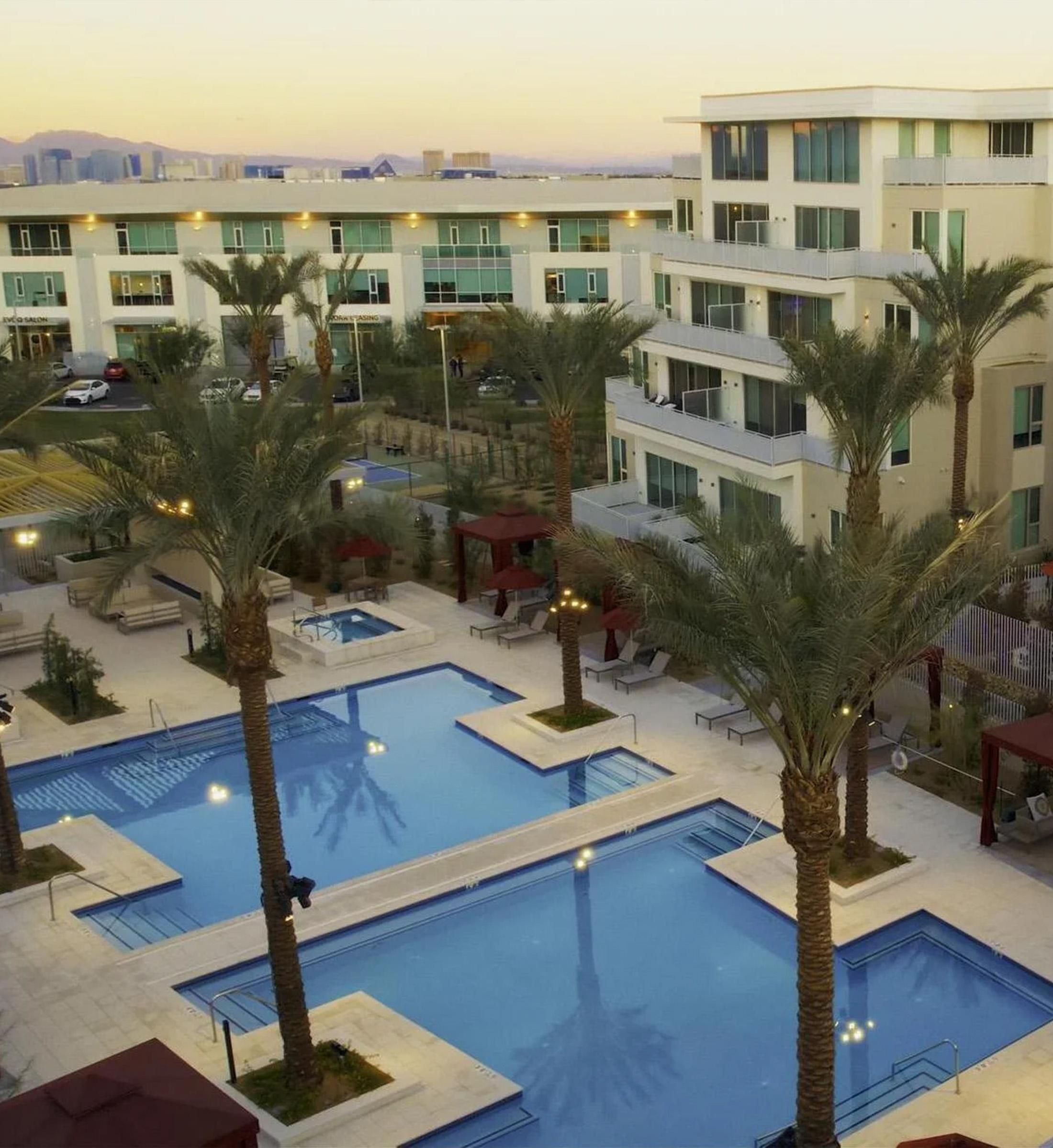 A modern apartment complex with palm trees and outdoor pools at sunset.