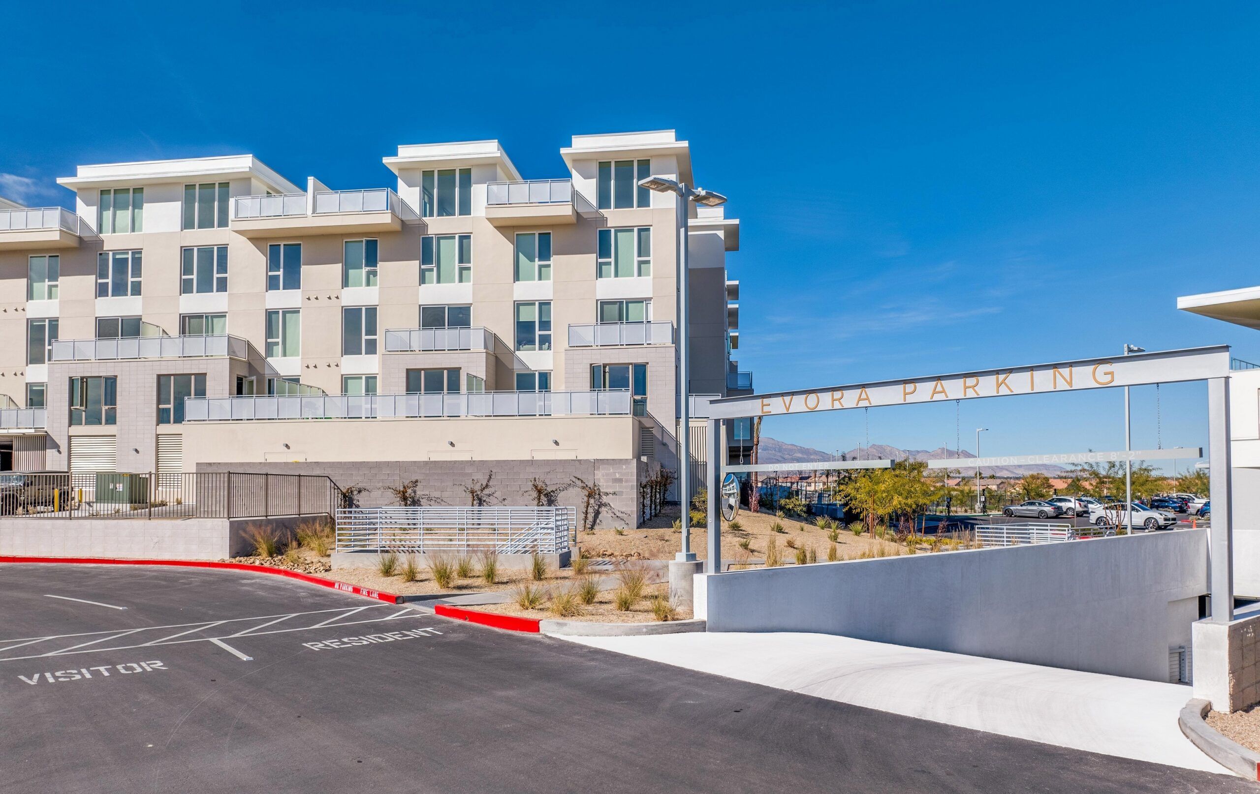 Modern apartment building with balconies, parking lot, and an entry sign reading “Evora Parking” on a sunny day.